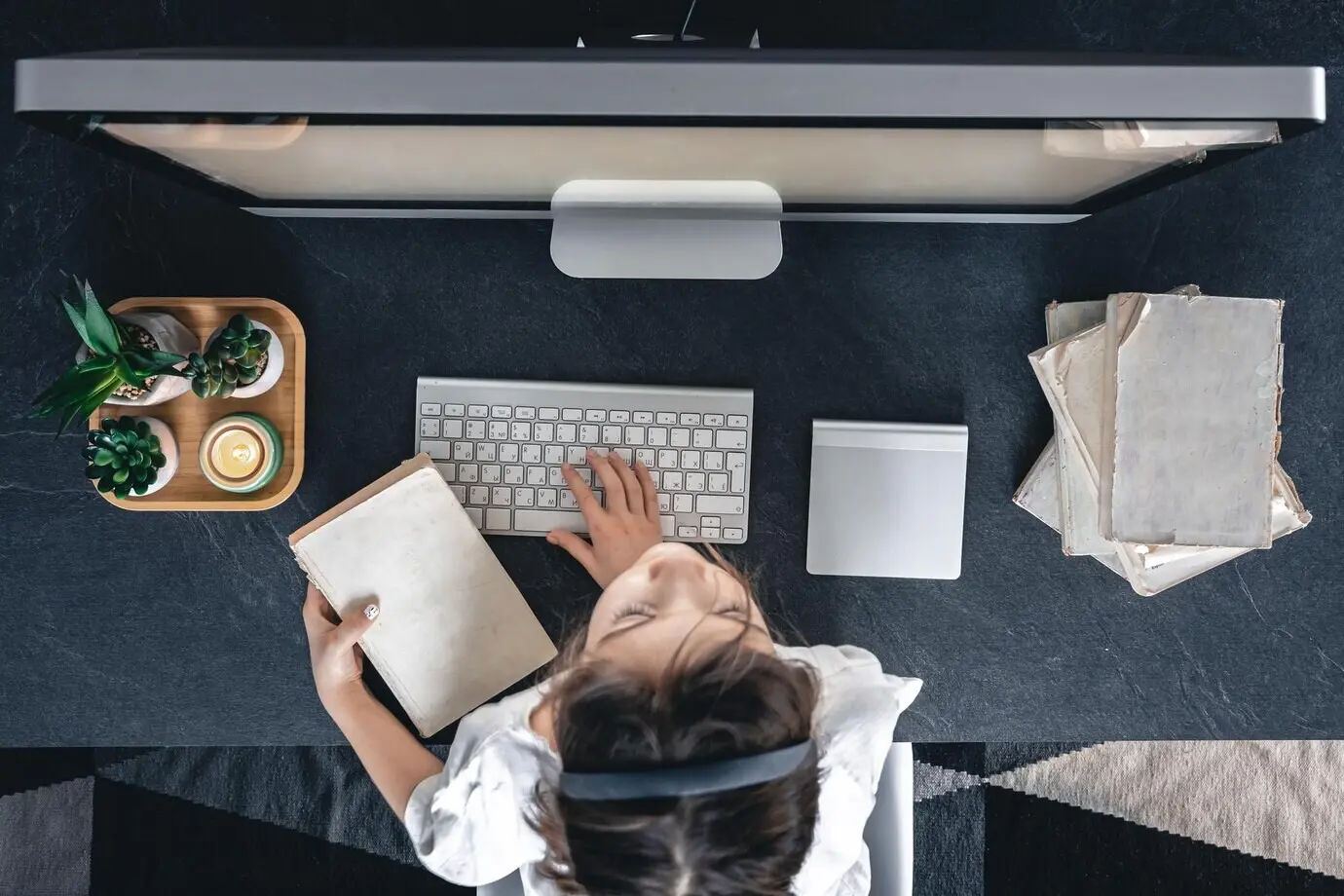 Top view of a little girl with books, sitting in front of a computer and studying.