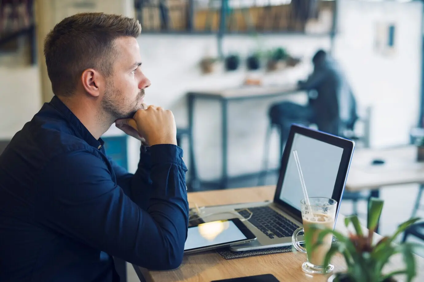 A young businessman sits in a cafe bar with a laptop, worried as he thinks about how to solve his problem.